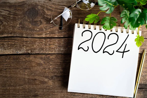 New year resolutions 2024 on desk. 2024 goals list with notebook, coffee cup, plant on wooden table. Resolutions, plan, goals, action, checklist, idea concept. New Year 2024 resolutions