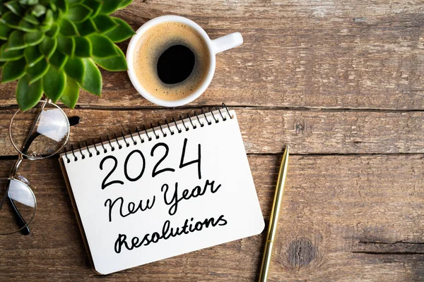 新年の決議2024が机の上に ノートブック コーヒーカップ 木のテーブルに植える2024ゴールリスト チェックリスト アイデアコンセプト 新年2024決議 ストック画像