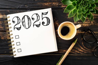 Yeni yıl kararları 2025 masada. 2025 gol listesi, defter, kahve fincanı, ahşap masa. Kararlar, plan, hedefler, eylem, kontrol listesi, fikir konsepti. Yeni yıl 2025 kararları. Boşluğu kopyala