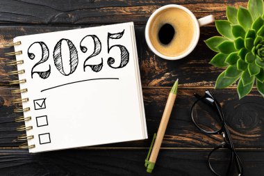 Yeni yıl kararları 2025 masada. Not defterli 2025 karar listesi, ahşap masadaki kahve fincanı. Hedefler, çözümler, plan, eylem, kontrol listesi konsepti. Yeni Yıl 2025 şablonu, kopyalama alanı