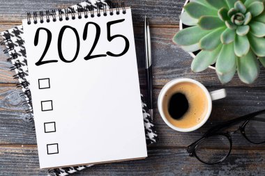 Yeni yıl kararları 2025 masada. 2025 gol listesi, defter, kahve fincanı, ahşap masa. Kararlar, plan, hedefler, eylem, kontrol listesi, fikir konsepti. Yeni yıl 2025 kararları. Boşluğu kopyala