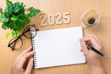 Yeni yıl kararları 2025 masada. 2025 gol - eller ve defter, kahve fincanı, ahşap masaya bitki. Çözümler, plan, hedefler, eylem, fikir konsepti. Yeni Yıl 2025 kararları, kopyalama alanı