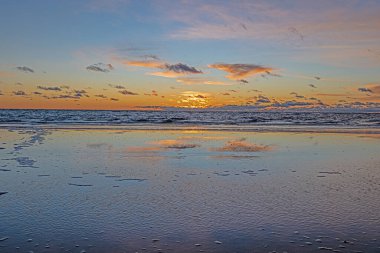 Kışın yükselen dalgalarda yansımalarla denizin üzerinde gün batımı