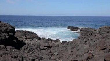 Gündüz vakti Lanzarote 'deki El Golfo yakınlarındaki volkanik kıyılarda sörf videosu.