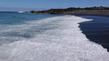 Gündüz vakti Lanzarote 'deki El Golfo yakınlarındaki volkanik kıyılarda sörf videosu.