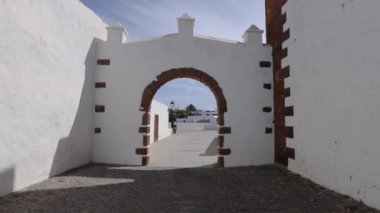 Gündüz vakti Lanzarote 'nin tarihi Teguise kasabasındaki eski bir beyaz taş duvardaki kemer yolunun videosu.