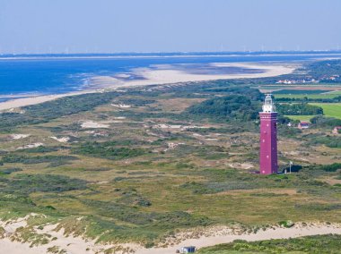 Hollanda 'daki Ouddorp deniz fenerinin gündüz vakti çevresindeki kum tepeleriyle drone fotoğrafı.