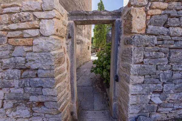 View through an old stone door frame without a door into a backyard of an ancient building during the day