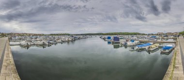 Yazın bulutlu gökyüzünün önünde rıhtıma yanaşmış gemilerin olduğu bir yat limanına bak.