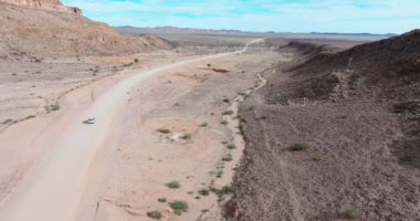 Yaz aylarında Namibya 'nın güneyindeki bir çöl bölgesinde çakıllı yolda giden dört tekerli bir aracın insansız hava aracı videosu.
