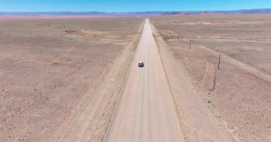 Namibya 'daki Namibya' daki Namib-Naukluft Ulusal Parkı 'nın kenarındaki çölde çakıllı bir yolda hareket halindeki bir aracın videosu.