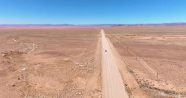 Namibya 'daki Namibya' daki Namib-Naukluft Ulusal Parkı 'nın kenarındaki çölde çakıllı bir yolda hareket halindeki bir aracın videosu.