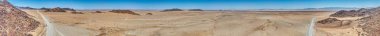 Gündüz vakti Namibya 'daki Namib-Naukluft Ulusal Parkı' nın kenarındaki çölde yalnız çakıl yolunun panoramik robot resmi.