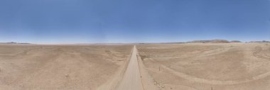 Gündüz vakti Namibya 'daki Namib-Naukluft Ulusal Parkı' nın kenarındaki çölde yalnız çakıl yolunun panoramik robot resmi.