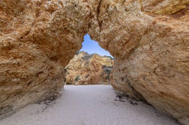 Uçsuz bucaksız bir çöl manzarasının ortasına kurulmuş şaşırtıcı derecede güzel, kemerli bir kaya oluşumu. Mavi gökyüzü ile çelişen altın kum.