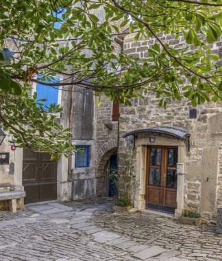 A cobblestone alleyway with a wooden door and window shutters in a bold blue hue, illuminated by a streetlamp clipart