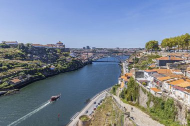 Bu resim hareketli bir şehir boyunca akan sakin bir nehri betimliyor, yemyeşil bir ormanı ve güzel bir arkaplanı var.