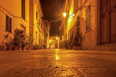 Tarihi bir İspanyol köyünde, gece vakti yapay ışıkta terk edilmiş bir caddenin görüntüsü.