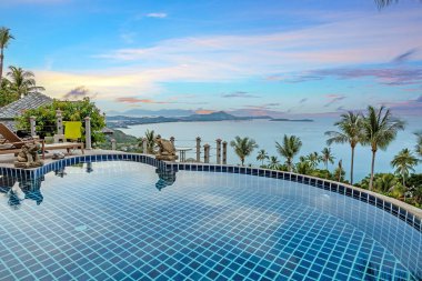 Akşam ışığında tropik bir plajın üzerindeki sonsuz bir havuza bak.