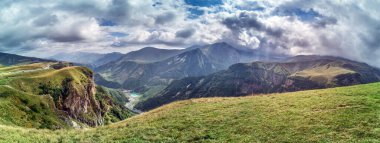 Scenic view of the Cross Pass in Georgia, showcasing lush green mountains and a winding valley during daytime clipart