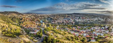 Tiflis, Gürcistan 'ın insansız hava aracı panoraması, güneş doğarken Kura Nehri ile birlikte yaz mevsiminde şehir manzarasını gözler önüne seriyor.