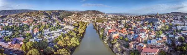 Tiflis, Gürcistan 'ın insansız hava aracı panoraması, güneş doğarken Kura Nehri ile birlikte yaz mevsiminde şehir manzarasını gözler önüne seriyor.