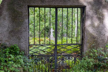 Kırsal demir kapı yemyeşil çimenler arasında gizli bir haç ortaya çıkarıyor. Gün ışığında huzur ve ruhsal cazibeyi yakalıyor.