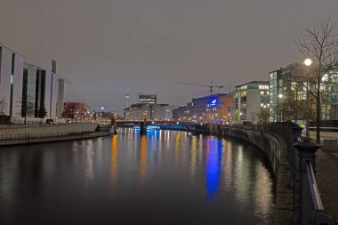 Berlin hükümet bölgesinin aydınlanmış modern mimarisi kışın Spree 'ye yansıyor.