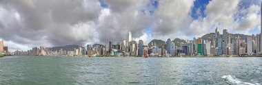 Panoramic daytime view of Hong Kong skyline, surrounded by lush green hills and a busy harbor in summer clipart