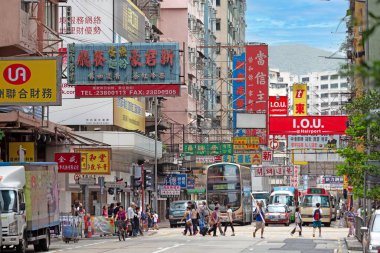 Hong Kong şehir merkezinde yayaların geçtiği, otobüslerin ve tabelaların olduğu hareketli sokak manzarası.