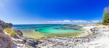 Turkuvaz suları ve Rottnest Adası 'ndaki kayalık kıyı şeridi ile gündüz vakti masmavi gökyüzünün altında