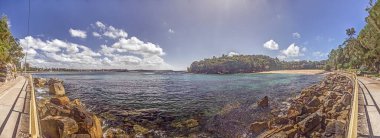 2015 'te Sydney' de güneşli gökyüzünün altında kumlu kıyılar, kayalar ve turkuaz sularla Manly Sahili manzarası