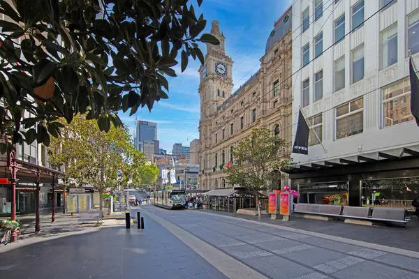 Gündüz vakti gelenek ve modernliği birleştiren ikonik tramvayla ve tarihi saat kulesiyle dolu Melbourne caddesi sahnesi