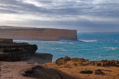 Büyük Okyanus Yolu 'nun yanındaki dramatik sahil kayalıkları ve okyanus manzarası. Gün boyunca bulutlu gökyüzü.