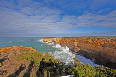 Büyük Okyanus Yolu 'nun yanındaki dramatik sahil kayalıkları ve okyanus manzarası. Gün boyunca bulutlu gökyüzü.
