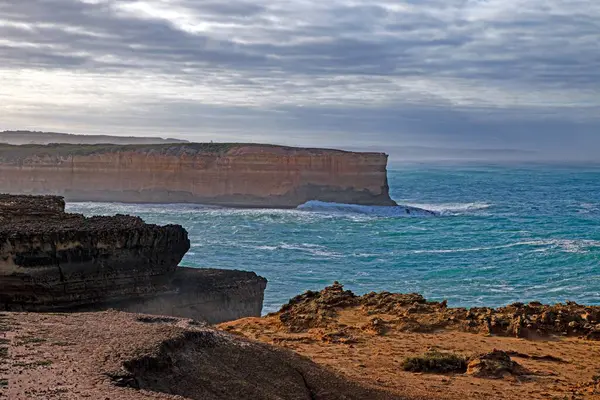 Büyük Okyanus Yolu 'nun yanındaki dramatik sahil kayalıkları ve okyanus manzarası. Gün boyunca bulutlu gökyüzü.
