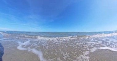 Dalgalar kumlu bir sahile alçak bir perspektiften çarpıyor. Gün ışığında doğal sahil güzelliğini vurguluyor.