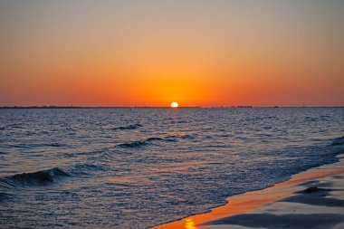 Canlı turuncu gökyüzü, yumuşak dalgalar ve Florida 'daki sakin sahil şeridiyle nefes kesici okyanus batımı.