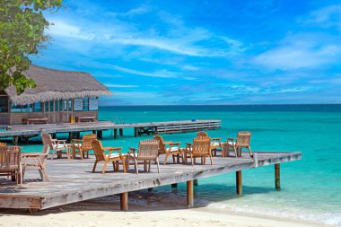 Tropical overwater bungalow with wooden deck turquoise ocean and scenic blue sky in daylight clipart