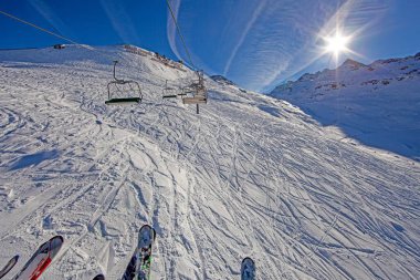 Chairlift over snowy slopes with skiers and clouds in Kleinwalsertal during daytime clipart