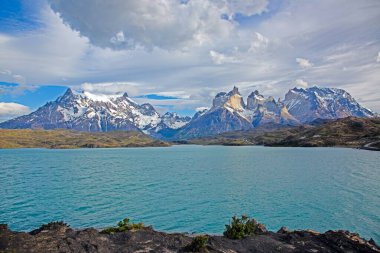Gündüz vakti Torres del Paine 'deki dramatik dağların ve geniş gökyüzünün yansımalarıyla Pehoe Gölü' nün panoramik görüntüsü