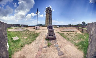 Galle Kalesi 'ndeki eski top ve saat kulesinde Sri Lanka bayrağı var, gündüz vakti kimse görünmüyor.