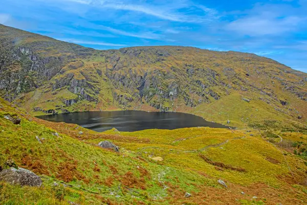 Derin dağ vadisindeki karanlık göl parlak mavi gökyüzünün altında kırsal İrlanda çöllerinde gündüz vakti