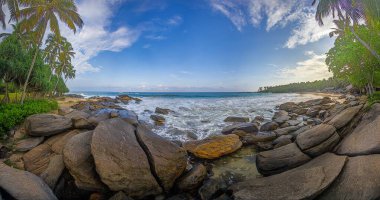 Gündüz vakti Goyambokka Sahili 'nde okyanus dalgaları ve sakin akşam ışığı olan Rocky plajı.