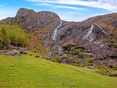 Akan şelalesi, ormanı ve manzaralı tepelerdeki kayalık arazisi olan yeşil vadi.