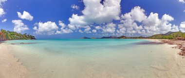Güneşli mavi gökyüzünün altında altın kumu ve turkuaz suyu olan tropik bir sahil.