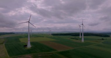 Bulutlu bir gökyüzünün altında dönen rüzgar türbinlerinin temiz enerjiyi ve kırsal sürdürülebilirliği vurgulayan hava zaman çizelgesi görüntüleri
