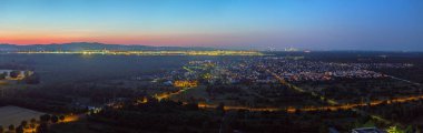 Wide aerial view over Frankfurt Airport and skyline at dusk with lights and distant mountains
