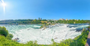 Schaffhausen İsviçre 'de açık gökyüzü ve yeşil ağaçlarla Ren Şelalesi' nin parlak güneşli manzarası