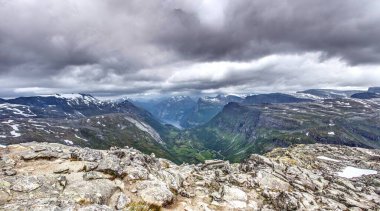 Kartal yolundaki Oernesvingen bakış açısından dramatik uçurumlar vadisiyle Geirangerjord üzerinde ve fırtınalı gökyüzü altında yedi kız kardeş şelalesi